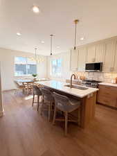 Dual tone kitchen featuring an island with sink, tasteful backsplash, stainless steel appliances, light stone countertops, and a kitchen bar