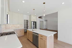 Kitchen with a center island with sink, tasteful backsplash, appliances with stainless steel finishes, light wood finished floors, and hanging light fixtures