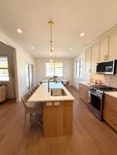 Dual tone kitchen with stainless steel appliances, pendant lighting, backsplash, a breakfast bar area, and light wood-type flooring