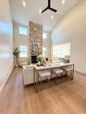 Living room featuring a ceiling fan, a stone fireplace, light wood-type flooring, vaulted ceiling, and recessed lighting