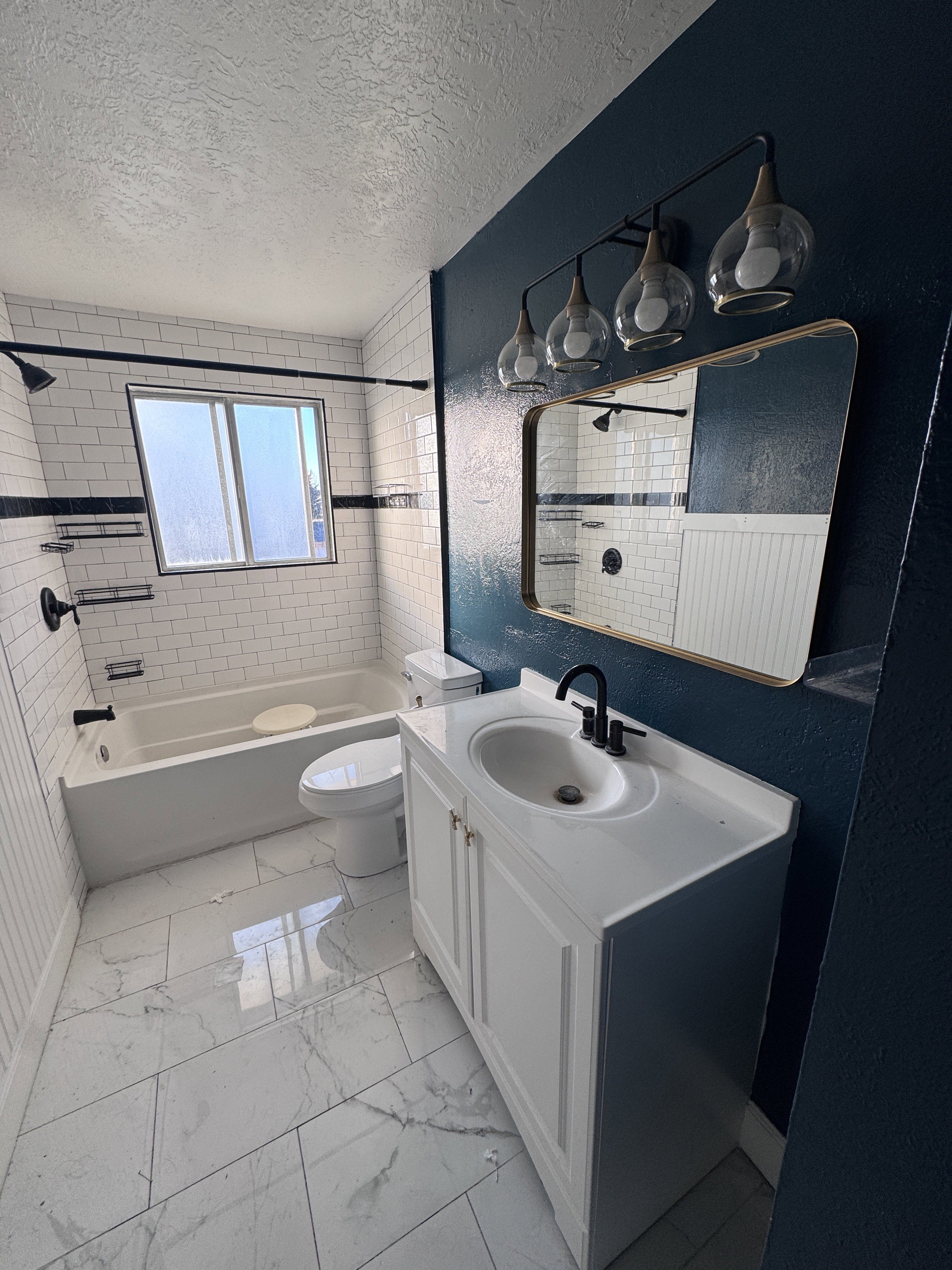 Full bath featuring washtub / shower combination, a textured ceiling, vanity, light marble finish floors, and a textured wall