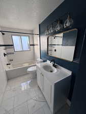 Full bath featuring washtub / shower combination, a textured ceiling, vanity, light marble finish floors, and a textured wall
