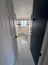 Bathroom with vanity, light marble finish floors, a textured ceiling, and shower / bath combination