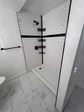 Bathroom featuring a textured wall, marble look tile flooring, a shower stall, and a textured ceiling