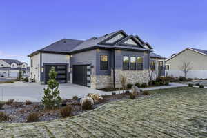 View of front of property featuring board and batten siding, stone siding, concrete driveway, a front yard, and a garage