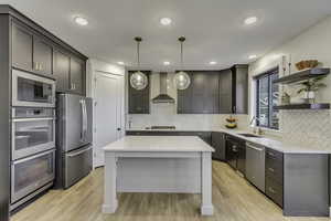Kitchen featuring open shelves, hanging light fixtures, stainless steel appliances, light stone counters, and light wood-style flooring