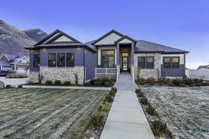 View of front of home with stone siding, a front lawn, and covered porch
