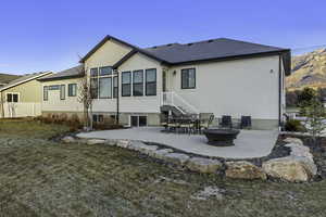 Rear view of property featuring a patio area, stucco siding, a fire pit, a lawn, and roof with shingles
