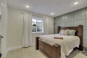 Bedroom featuring light colored carpet, a decorative wall, and recessed lighting