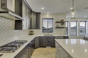 Kitchen featuring wall chimney range hood, decorative light fixtures, stainless steel appliances, light wood-style floors, and backsplash