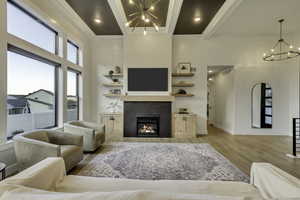 Living area with a chandelier, beam ceiling, light wood finished floors, a tiled fireplace, and a high ceiling