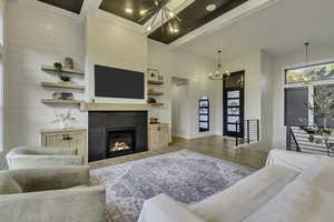 Living area featuring beam ceiling, a chandelier, light wood finished floors, a tiled fireplace, and a high ceiling