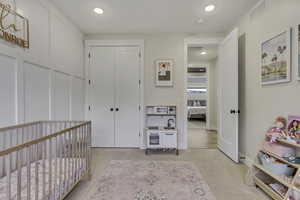 Bedroom featuring a nursery area, light colored carpet, recessed lighting, and a closet