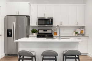Kitchen featuring stainless steel appliances, light wood finished floors, a kitchen island with sink, and a breakfast bar area