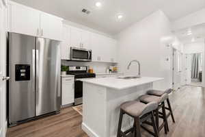 Kitchen featuring appliances with stainless steel finishes, dark wood finished floors, an island with sink, white cabinets, and recessed lighting