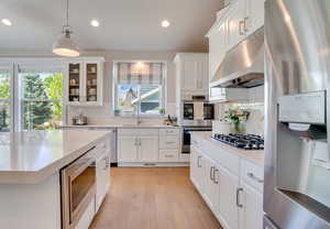 Kitchen with appliances with stainless steel finishes, pendant lighting, under cabinet range hood, white cabinets, and glass insert cabinets