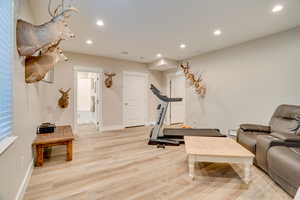 Exercise room with light wood-style floors and recessed lighting