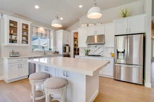 Kitchen with stainless steel appliances, a breakfast bar area, decorative light fixtures, under cabinet range hood, and lofted ceiling