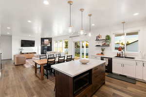 Kitchen featuring decorative light fixtures, white cabinets, open floor plan, stainless steel microwave, and wood-type flooring
