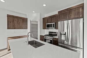 Kitchen featuring stainless steel appliances, tasteful backsplash, light stone counters, dark brown cabinets, and recessed lighting