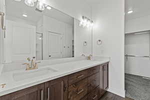 Primary bathroom with a spacious closet, double vanity, recessed lighting, an enclosed shower, and dark wood-type flooring