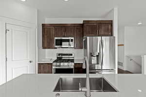 Kitchen with stainless steel appliances, dark brown cabinetry, decorative backsplash, light stone countertops, and recessed lighting