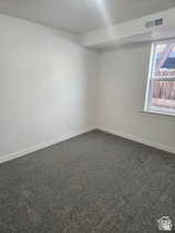 Spare room featuring dark colored carpet and baseboards