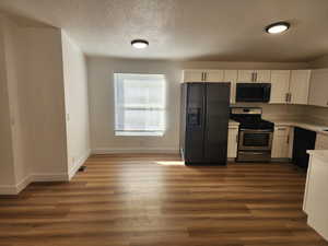 Kitchen featuring black appliances, white cabinets, dark wood-style flooring, a textured ceiling, and light stone countertops