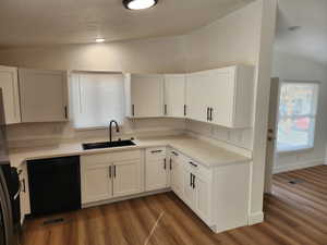 Kitchen featuring vaulted ceiling, black appliances, white cabinets, dark wood-type flooring, and a textured ceiling