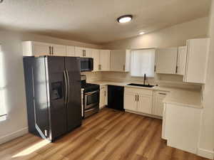 Kitchen with black appliances, white cabinets, lofted ceiling, light wood-type flooring, and a textured ceiling