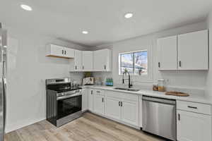 Kitchen with stainless steel appliances, white cabinetry, light stone countertops, light wood finished floors, and recessed lighting