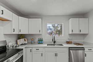 Kitchen featuring stainless steel appliances, white cabinetry, and light stone counters