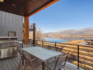 Wooden terrace featuring outdoor dining area, a water and mountain view, and exterior kitchen