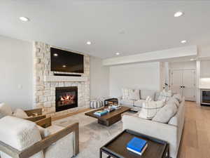Living area with a stone fireplace, light wood-style flooring, beverage cooler, and recessed lighting