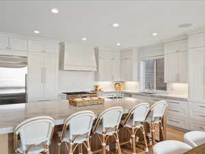 Kitchen featuring built in refrigerator, premium range hood, light stone countertops, white cabinetry, and recessed lighting