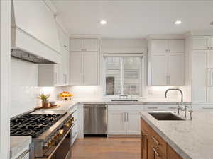Kitchen featuring brown cabinets, stainless steel appliances, premium range hood, light wood-style floors, and white cabinets