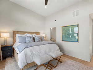 Bedroom with light wood finished floors, ensuite bath, ceiling fan, and high vaulted ceiling