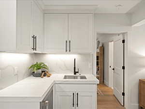 Bar area with white cabinets, tasteful backsplash, light wood-style flooring, and light stone counters