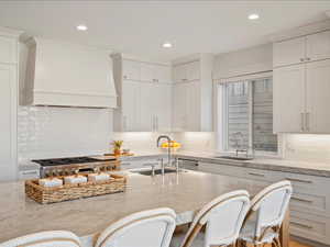Kitchen with custom exhaust hood, light stone countertops, decorative backsplash, and recessed lighting