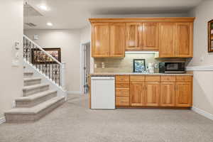 Kitchen with white dishwasher, light carpet, decorative backsplash, black microwave, and brown cabinets