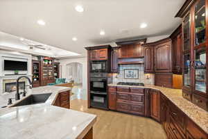 Kitchen with arched walkways, a glass covered fireplace, black appliances, light stone counters, and open floor plan