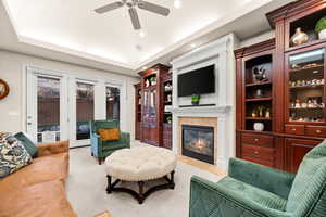 Living area with a glass covered fireplace, a tray ceiling, light carpet, and a ceiling fan