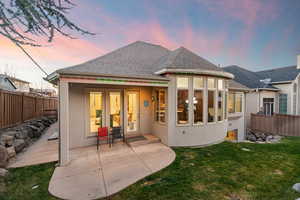 Back of property at dusk with stucco siding, roof with shingles, and a fenced backyard