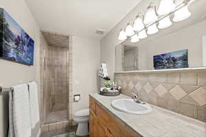 Bathroom with backsplash, a stall shower, vanity, and dark tile patterned floors
