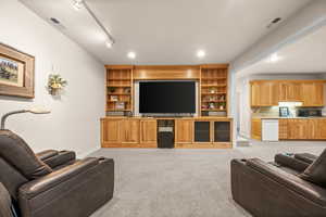 Living area featuring rail lighting, light colored carpet, and built in shelves