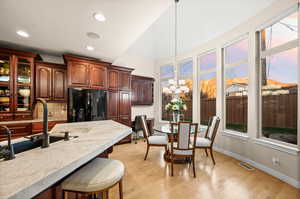 Kitchen with decorative light fixtures, black refrigerator with ice dispenser, tasteful backsplash, light stone counters, and glass insert cabinets