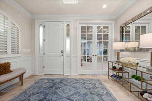 Foyer with a decorative wall, wainscoting, ornamental molding, plenty of natural light, and french doors