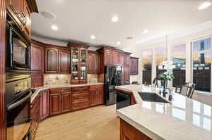 Kitchen with pendant lighting, light stone countertops, tasteful backsplash, black appliances, and light wood-style floors