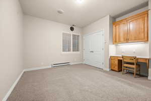 Unfurnished office with light carpet, built in study area, and a baseboard radiator