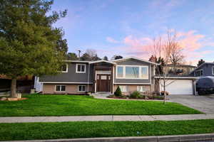 Split foyer home featuring brick siding, a yard, concrete driveway, a garage, and a chimney